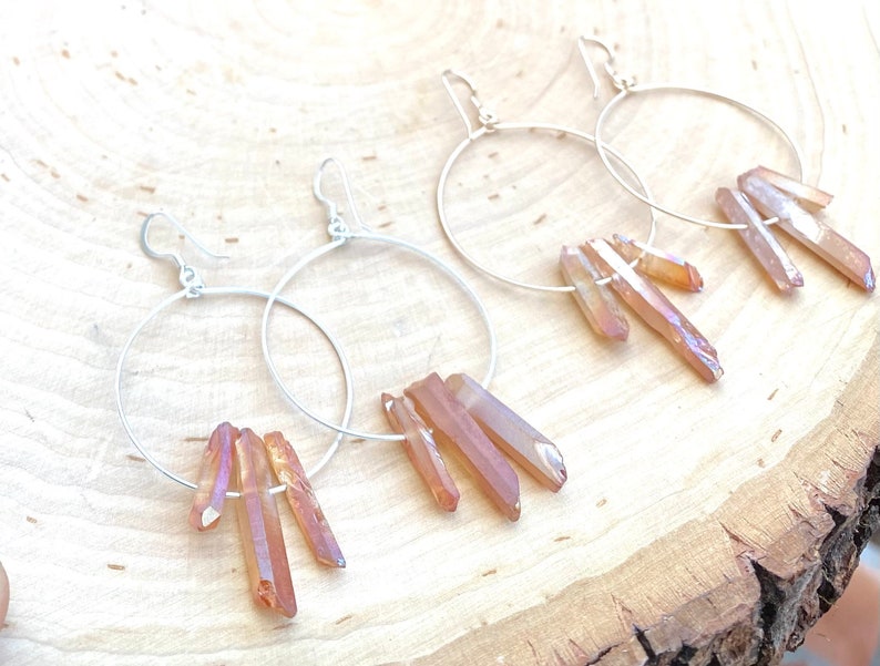 May include: A pair of silver hoop earrings with dangling iridescent orange crystal points.