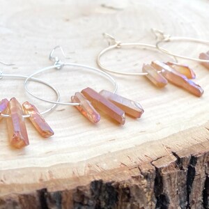 May include: A pair of silver hoop earrings with three iridescent orange crystal points dangling from each hoop.