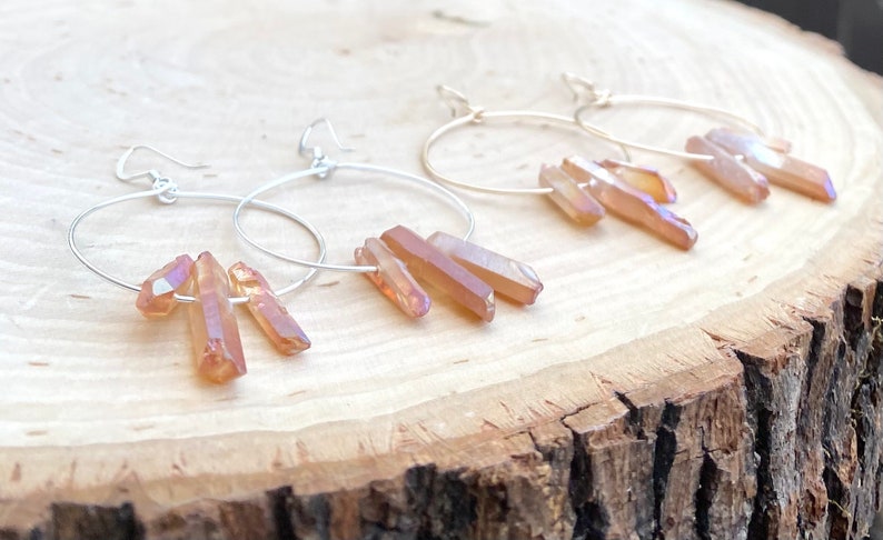 May include: A pair of silver hoop earrings with three iridescent orange crystal points dangling from each hoop.