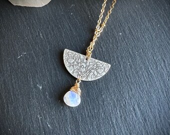 May include: A gold chain necklace with a silver half-moon pendant featuring a textured design and a white moonstone drop.