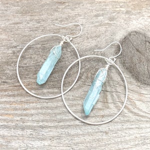 Puede incluir: Pendientes de aro de plata con un colgante de cristal azul claro que cuelga de cada aro.