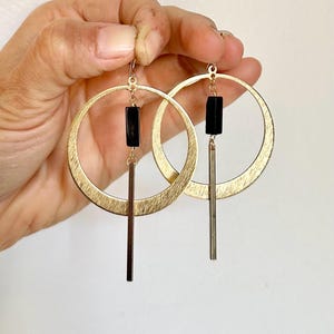 May include: Gold hoop earrings with a black rectangular bead and a long, thin gold bar hanging from the bottom.