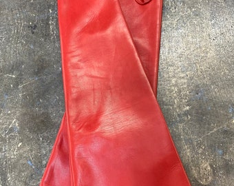 Op de afbeelding: Een paar lange, rode leren handschoenen met een klein geborduurd logo op de manchet.