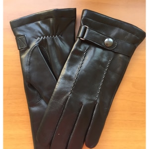 Op de afbeelding: Een paar zwarte leren handschoenen. De handschoenen hebben een gestikt ontwerp en een bandje met een zilveren knoopsluiting. De handschoenen zijn gemaakt van glad, glanzend leer.