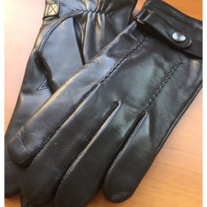 Op de afbeelding: Een paar zwarte leren handschoenen. De handschoenen hebben een klassiek ontwerp met een knoopsluiting bij de pols en decoratieve stiksels. Het leer ziet er glad en soepel uit, wat wijst op een hoogwaardig product.