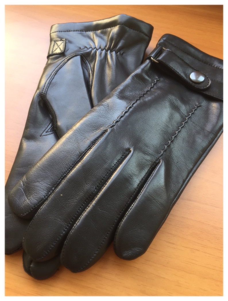 Op de afbeelding: Een paar zwarte leren handschoenen. De handschoenen hebben een klassiek ontwerp met een knoopsluiting bij de pols en decoratieve stiksels. Het leer ziet er glad en soepel uit, wat wijst op een hoogwaardig product.