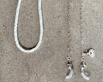 May include: Two eyeglass chains, one made of white beads and the other a silver chain with a silver lotus charm and clear plastic ends.