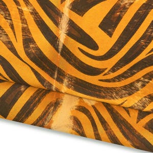 May include: Close-up of a fabric with a tiger stripe pattern. The fabric features alternating bands of dark brown and golden yellow, creating a bold and striking design. The material is folded over, revealing the pattern's texture.