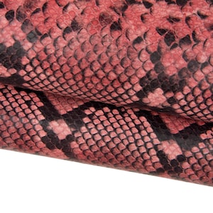 Könnte beinhalten: Nahaufnahme eines strukturierten Schlangenmuster in Rot- und Schwarztönen. Die Schuppen sind dicht gepackt und erzeugen ein detailliertes und visuell auffälliges Design. Das Material scheint gefaltet zu sein und zeigt die Unterseite der Haut.