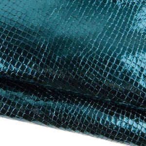 May include: Close-up of a teal-coloured, textured material with a reptile-like pattern. The surface has a glossy sheen, reflecting light and creating highlights and shadows. The material appears to be folded, revealing its depth and texture.