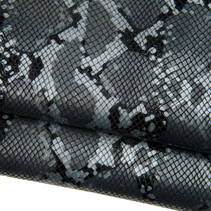 May include: Close-up of a textured material with a snakeskin pattern. The fabric features a repeating design of gray, white, and black scales. The material is folded, revealing the underside and adding depth to the image.