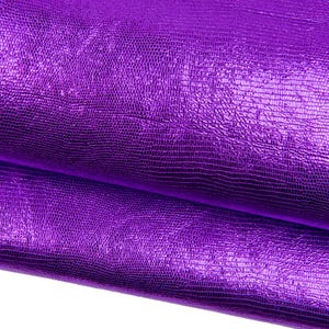 Puede incluir: Primer plano de una lámina de cuero sintético morado brillante y texturizado. El material tiene un patrón de escamas de reptil y un brillo metálico. La tela está doblada, revelando el reverso.
