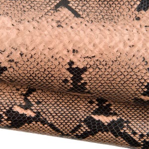 Könnte beinhalten: Nahaufnahme eines strukturierten Materials mit Schlangenmuster. Das Design zeigt ein sich wiederholendes Schuppenmuster in Schwarz und Beige, wodurch ein realistischer Reptilienhaut-Effekt entsteht. Das Material scheint flexibel zu sein und möglicherweise Leder oder ein lederähnliches Produkt.