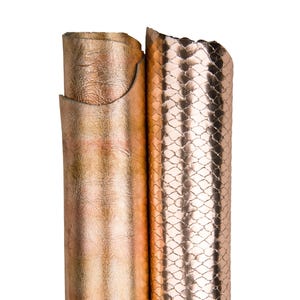 Może przedstawiać: Dwie rolki metalicznej skóry w odcieniach miedzi i różowego złota. Lewa rolka ma gładką fakturę, prawa wzór przypominający łuski. Skóra jest ciasno zwinięta, ukazując elastyczność i połysk.