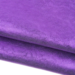 Könnte beinhalten: Nahaufnahme eines leuchtend lila Stoffes mit einem strukturierten, schuppenartigen Muster. Das Material ist gefaltet und zeigt Schichten der schimmernden, irisierenden Oberfläche. Die Textur und Farbe des Stoffes deuten darauf hin, dass er für Mode- oder Dekorationszwecke verwendet werden könnte.