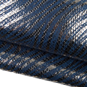 Puede incluir: Primer plano de cuero texturizado azul y plateado. El cuero tiene un patrón de piel de serpiente con rayas plateadas diagonales sobre un fondo azul. El material está doblado, mostrando la textura y el brillo.