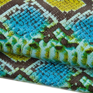 Puede incluir: Primer plano de un material texturizado con un patrón de piel de serpiente. El diseño presenta un patrón repetitivo de escamas en tonos de azul, amarillo y marrón. El material parece estar doblado, revelando la parte inferior.