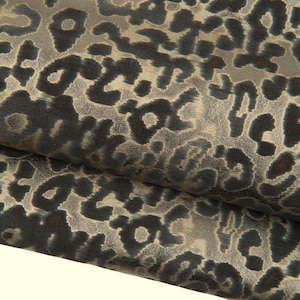 Può includere: Primo piano di un tessuto con motivo leopardato. Il design presenta macchie grigio scuro su uno sfondo grigio chiaro. Il tessuto è piegato, rivelando la sua consistenza e la ripetizione del motivo. Ideale per la moda o l'arredamento.