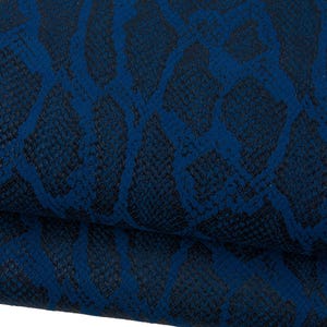 Op de afbeelding: Close-up van een gevouwen stuk stof met een donkerblauw slangenleerpatroon. Het patroon heeft een netwerk van onderling verbonden vormen in een lichtere blauwtint, waardoor een textuur ontstaat. De stof lijkt leer te zijn.