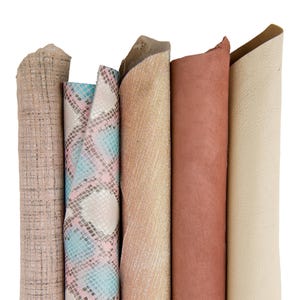 Może przedstawiać: Pięć różnych rolek tkaniny w różnych kolorach i wzorach. Tkaniny obejmują jasnobrązową tkaninę z tkanym wzorem, różową i niebieską tkaninę ze wzorem skóry węża, jasnobrązową tkaninę z tkanym wzorem, czerwonobrązową tkaninę i jasnobeżową tkaninę.