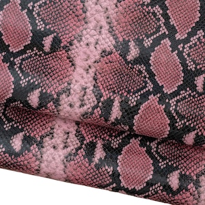 Könnte beinhalten: Nahaufnahme von rosa und schwarzem Schlangenleder. Das Leder hat eine strukturierte Oberfläche mit einem sich wiederholenden Schuppenmuster. Die rosa Farbe ist ein weicher, gedämpfter Farbton, und das Schwarz sorgt für Kontrast. Das Leder ist über sich selbst gefaltet.
