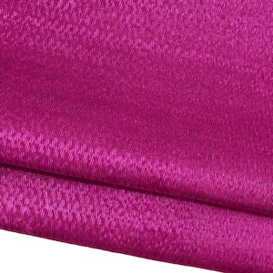 Puede incluir: Primer plano de una tela magenta doblada. El material tiene una superficie texturizada y acanalada, con un brillo sutil. Los pliegues crean sombras y reflejos, realzando la profundidad y la textura de la tela. La tela parece suave, posiblemente seda o satén.