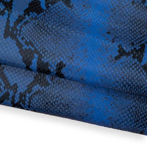 May include: Close-up of a textured, blue and black snakeskin pattern. The pattern features a scale-like design with varying shades of blue and black, creating a realistic reptile skin appearance. The material appears to be leather or a similar fabric.