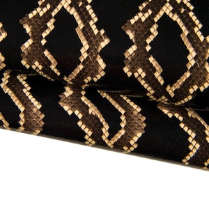 Könnte beinhalten: Nahaufnahme eines schwarzen und braunen Schlangenlederstoffs mit einem sich wiederholenden Rautenmuster.