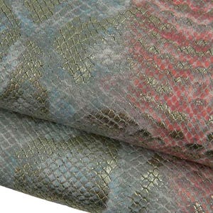 Peut inclure: Une pièce de matériau texturé pliée présentant un motif en peau de serpent avec une finition dorée métallique. La surface affiche un dégradé de couleurs incluant du bleu sourd, du gris doux et du rose corail vif, créant un aspect multicolore.