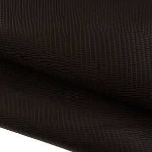 May include: A dark brown material featuring a textured surface with a repeating pattern of small, rectangular scales. The material is folded over itself, creating a soft curve and showing the consistent embossed finish across the entire surface.