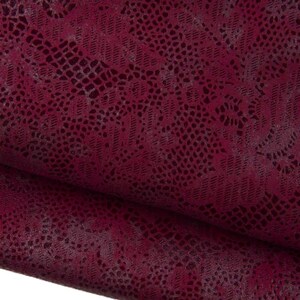 May include: A deep burgundy fabric featuring a dark, intricate lace pattern overlaid on the surface. The material displays a textured appearance with a repeating floral motif, creating a layered visual effect across the folded textile surface.