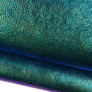 Op de afbeelding: Een vel gestructureerd materiaal met een metallic, iriserende afwerking die verschuift tussen diepe tinten blauw, levendig turkoois en vleugjes paars. Het oppervlak vertoont een fijn, korrelig patroon dat het licht vangt over de plooien heen.