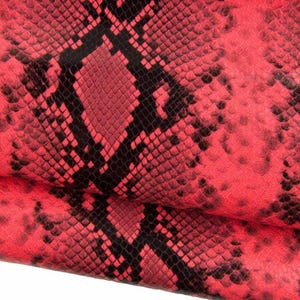 May include: Close-up of red and black snakeskin pattern. The pattern features a repeating scale design in shades of red and black, creating a textured appearance. The image shows a close-up of the snakeskin, highlighting the intricate details and color variations.