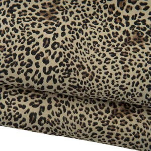 Puede incluir: Primer plano de una tela con estampado de leopardo. La tela tiene un fondo beige con manchas marrones oscuras y negras. La tela está doblada, mostrando el patrón en detalle.