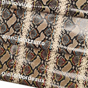 Pode incluir: Close-up de um tecido com um padr&atilde;o de pele de cobra em tons de marrom, preto, amarelo, laranja, azul e roxo. O tecido est&aacute; dobrado, revelando diferentes combina&ccedil;&otilde;es de cores.