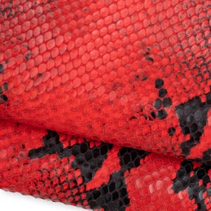 May include: A textured material featuring a vibrant red and black snakeskin pattern. The surface displays a repeating scale-like design with deep black patches interspersed throughout the bright red base, creating a high-contrast visual effect.