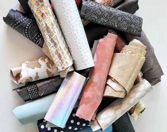 Pode incluir: Uma coleção de amostras de tecido em várias cores e padrões, incluindo preto, branco, dourado, vermelho e azul. As amostras estão enroladas e dispostas em uma pilha.