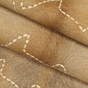 May include: Close-up of a brown cowhide rug with white stitching in a wavy pattern.