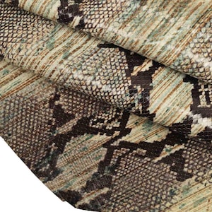 May include: Close-up of a folded piece of fabric with a snakeskin pattern. The fabric features a mix of brown, black, and green hues, creating a realistic reptile skin effect. The texture appears detailed and slightly rough.