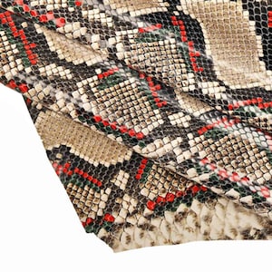 Peut inclure: Gros plan sur un tissu en peau de serpent avec un motif de carrés rouges, verts et noirs sur un fond beige. Le tissu est plié sur lui-même, créant un effet texturé.