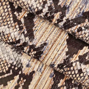 Op de afbeelding: Close-up van een stof met een slangenhuidpatroon in tinten bruin, beige en blauw.