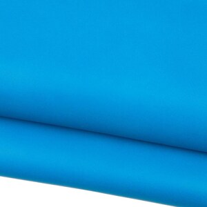 May include: A close-up shot of a vibrant, solid turquoise fabric. The fabric is folded over, creating a layered effect. The color is consistent throughout the image, with no visible patterns or textures.