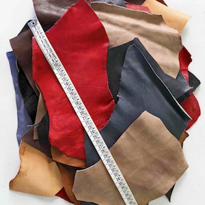 Pode incluir: Um monte de sobras de couro em v&aacute;rias cores, incluindo vermelho, marrom, bege e azul. Uma fita m&eacute;trica est&aacute; sobre o couro.