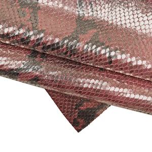 Puede incluir: Primer plano de una tela de piel de serpiente rosa y plateada con un patrón texturizado. La tela está doblada sobre sí misma, mostrando los diferentes colores y texturas.