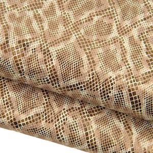 Op de afbeelding: Een gevouwen stuk materiaal met een herhalend geometrisch rasterpatroon in tinten beige, lichtbruin en donkerbruin. Het oppervlak heeft een getextureerd uiterlijk met een subtiele metallic glans, wat een gestructureerde look geeft aan de plooien.