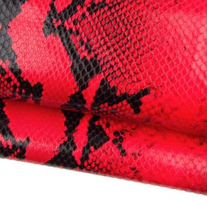 May include: Close-up of a vibrant red and black snakeskin pattern. The design features a repeating scale pattern in a bold colour combination, creating a striking visual texture. The material appears to be leather or a similar textile.
