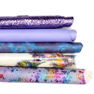 Op de afbeelding: Een stapel van vijf opgerolde vellen materiaal. De bovenste rol is metallic paars met een slangenhuistextuur. Daaronder ligt een gladde lichtlavendelkleurige rol, gevolgd door een blauwe slangenhuistextuur, een witte rol met een kleurrijke verenprint en een lichtpaarse rol met een veelkleurig gespikkeld patroon.