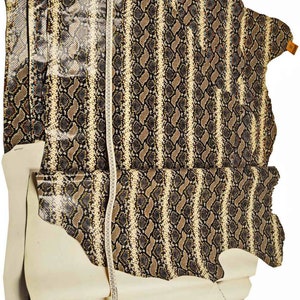 Pode incluir: Um peda&ccedil;o de couro de cobra bege e marrom com um padr&atilde;o listrado. O couro &eacute; medido com uma fita m&eacute;trica.