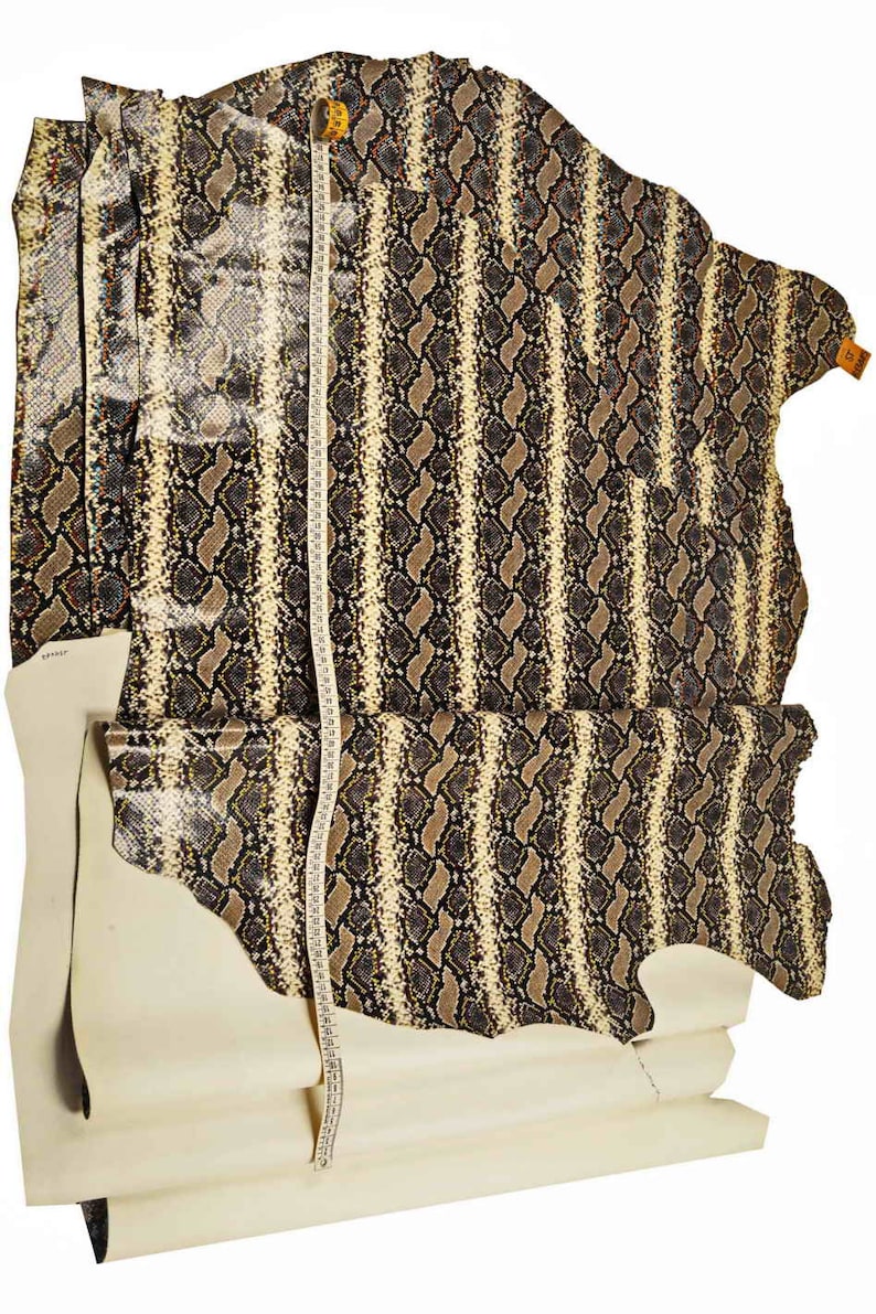 Pode incluir: Um peda&ccedil;o de couro de cobra bege e marrom com um padr&atilde;o listrado. O couro &eacute; medido com uma fita m&eacute;trica.