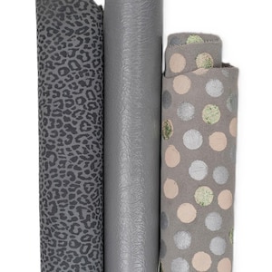 May include: Three vertical rolls of fabric. The left roll is dark gray with a black leopard print. The center roll is a solid, smooth, light gray material. The right roll is a light gray fabric featuring a pattern of silver and pale green dots.